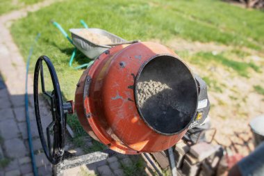 Çimento karıştırıcısı dışarıda çalışıyor. Yakınlarda taze beton ve kova var.