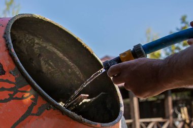 Çimento karıştırıcısı dışarıda çalışıyor. Yakınlarda taze beton ve kova var.