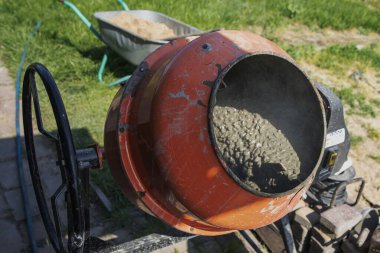 Çimento karıştırıcısı dışarıda çalışıyor. Yakınlarda taze beton ve kova var.