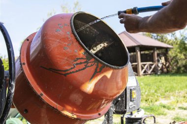 Çimento karıştırıcısı dışarıda çalışıyor. Yakınlarda taze beton ve kova var.