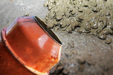 Çimento karıştırıcısı dışarıda çalışıyor. Yakınlarda taze beton ve kova var.