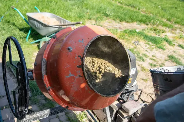 Çimento karıştırıcısı dışarıda çalışıyor. Yakınlarda taze beton ve kova var.