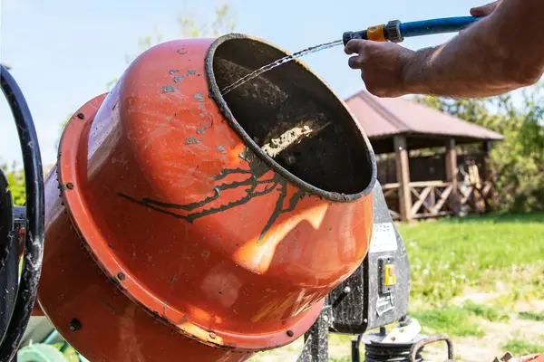 Çimento karıştırıcısı dışarıda çalışıyor. Yakınlarda taze beton ve kova var.
