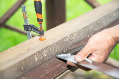 Açık havada tahta kiriş kesen bir adam. Klempler ve elektrikli aletlerle marangozluk işlemi. Ahşap işçiliği, işçiliği, ev yenilemesi ve DIY inşaatı kavramı.