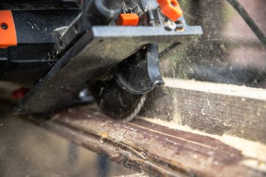 Açık havada tahta kiriş kesen bir adam. Klempler ve elektrikli aletlerle marangozluk işlemi. Ahşap işçiliği, işçiliği, ev yenilemesi ve DIY inşaatı kavramı.