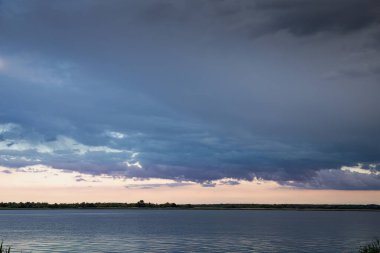 Akşam karanlığında sakin bir nehrin üzerinde dramatik bulutlu bir gökyüzü.