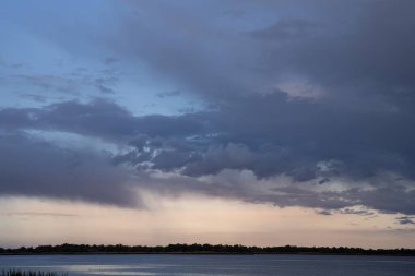 Akşam karanlığında sakin bir nehrin üzerinde dramatik bulutlu bir gökyüzü.