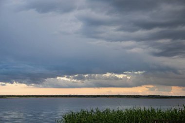 Akşam karanlığında sakin bir nehrin üzerinde dramatik bulutlu bir gökyüzü.