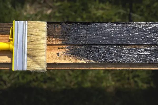 Kısmen boyanmış tahta üzerinde siyah koruyucu kaplamalı fırça.