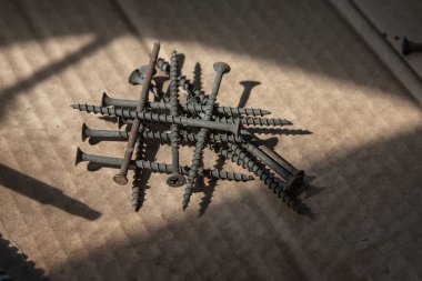 Güneş ışığı, inşaat ve onarım konseptinde karton yüzeyde siyah vidalar yığını