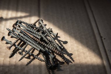 Güneş ışığı, inşaat ve onarım konseptinde karton yüzeyde siyah vidalar yığını