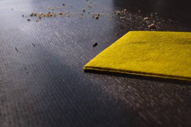 Sarı temizlik bezi ve siyah ahşap masadaki kırıntılar, ev temizliği kavramı.