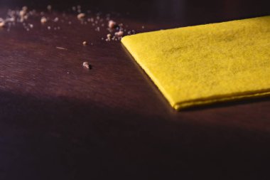 Sarı temizlik bezi ve siyah ahşap masadaki kırıntılar, ev temizliği kavramı.