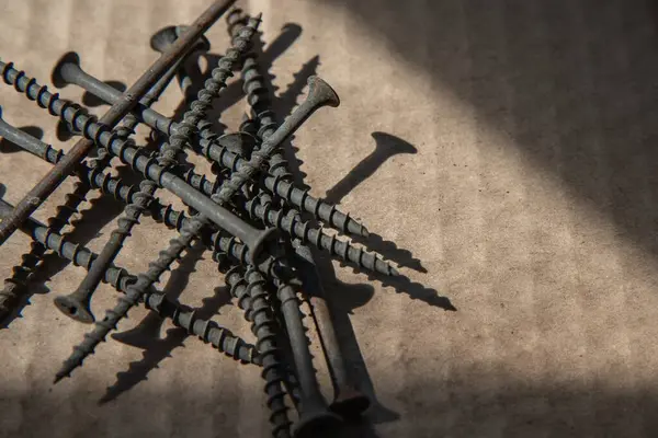 Güneş ışığı, inşaat ve onarım konseptinde karton yüzeyde siyah vidalar yığını