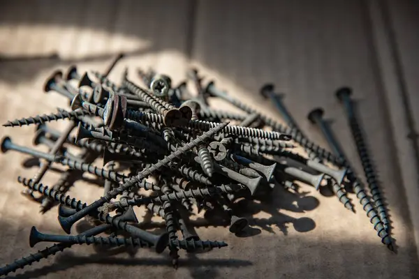 Güneş ışığı, inşaat ve onarım konseptinde karton yüzeyde siyah vidalar yığını