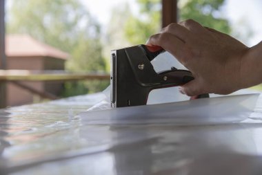 Atölyedeki tahta tahtada plastik çarşaf tamir etmek için zımba tabancası kullanan adam