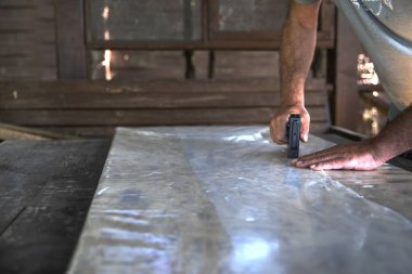 Atölyedeki tahta tahtada plastik çarşaf tamir etmek için zımba tabancası kullanan adam