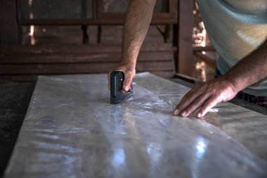 Atölyedeki tahta tahtada plastik çarşaf tamir etmek için zımba tabancası kullanan adam