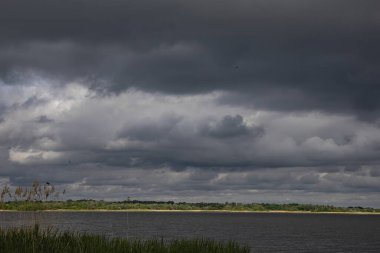 Nehir manzarası üzerinde dramatik fırtına bulutları ve ufukta güneş ışığı