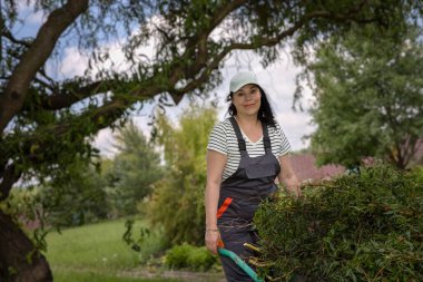 Arka bahçede ağaç dallarını budayan bir kadın.