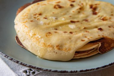 Eritilmiş tereyağlı lezzetli ev yapımı krepler, kırsal seramik tabakta servis ediliyor. Konforlu ev yemekleri ve konfor konsepti yumuşak, altın katmanlı.