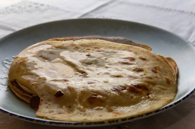 Üzerinde erimiş tereyağı olan ev yapımı krep yığınının yakın çekim görüntüsü, klasik mavi bir tabakta servis ediliyor. Geleneksel kahvaltı ya da tatlı konsepti yumuşak doku ve altın yüzey.