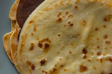 Üzerinde erimiş tereyağı olan ev yapımı krep yığınının yakın çekim görüntüsü, klasik mavi bir tabakta servis ediliyor. Geleneksel kahvaltı ya da tatlı konsepti yumuşak doku ve altın yüzey.