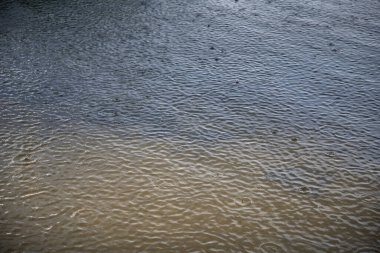 Yağmurlu bir günde dalgalı su yüzeyine düşen yağmur damlaları. Arka plan, hava durumu, sakinlik ve ruh hali temaları için doğal soyut doku.