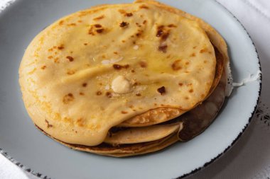 Eritilmiş tereyağlı lezzetli ev yapımı krepler, kırsal seramik tabakta servis ediliyor. Konforlu ev yemekleri ve konfor konsepti yumuşak, altın katmanlı.