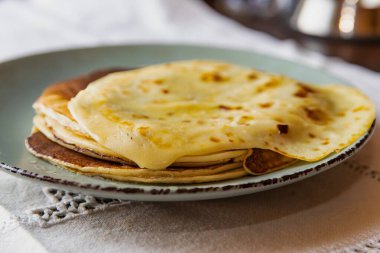 Eritilmiş tereyağlı lezzetli ev yapımı krepler, kırsal seramik tabakta servis ediliyor. Konforlu ev yemekleri ve konfor konsepti yumuşak, altın katmanlı.