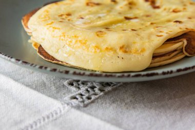 Üzerinde erimiş tereyağı olan ev yapımı krep yığınının yakın çekim görüntüsü, klasik mavi bir tabakta servis ediliyor. Geleneksel kahvaltı ya da tatlı konsepti yumuşak doku ve altın yüzey.