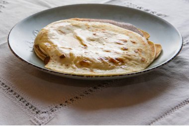 Eritilmiş tereyağlı lezzetli ev yapımı krepler, kırsal seramik tabakta servis ediliyor. Konforlu ev yemekleri ve konfor konsepti yumuşak, altın katmanlı.