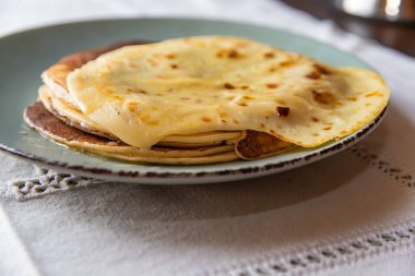 Üzerinde erimiş tereyağı olan ev yapımı krep yığınının yakın çekim görüntüsü, klasik mavi bir tabakta servis ediliyor. Geleneksel kahvaltı ya da tatlı konsepti yumuşak doku ve altın yüzey.