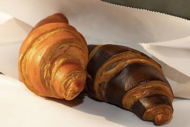 Beyaz kağıtta iki kruvasan, altın ve çikolata kabuğu.