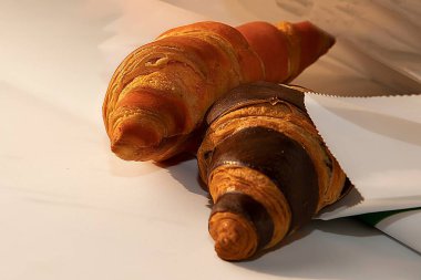 Beyaz kağıtta iki kruvasan, altın ve çikolata kabuğu.