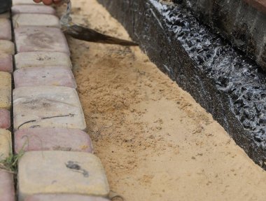 Siyah su geçirmez temellerin yakınındaki kum tabanına taş döşenmiş. Kentsel bahçe inşaatı, patika tesisatı, bina yenileme..