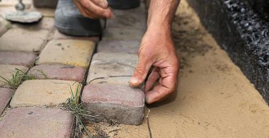 İşçi, su geçirmez temellerin yanındaki kum tabanına elle taş döşüyordu.