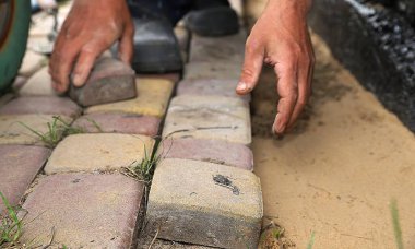 İşçi, su geçirmez temellerin yanındaki kum tabanına elle taş döşüyordu.