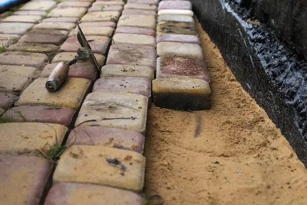İşçiler kumun üzerine tuğla dökerek su geçirmez ev temellerinin yanına tuğla döşüyorlar. İnşaat ve peyzaj süreci.