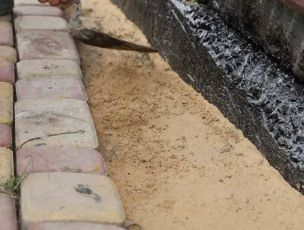 Siyah su geçirmez temellerin yakınındaki kum tabanına taş döşenmiş. Kentsel bahçe inşaatı, patika tesisatı, bina yenileme..