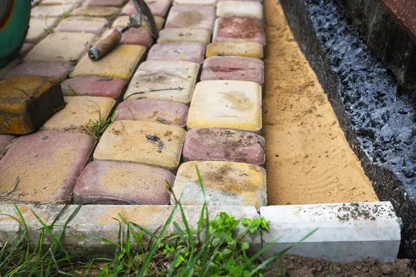 İşçiler kumun üzerine tuğla dökerek su geçirmez ev temellerinin yanına tuğla döşüyorlar. İnşaat ve peyzaj süreci.