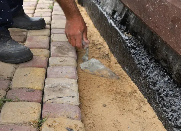 İşçi, su geçirmez temellerin yanındaki kum tabanına elle taş döşüyordu.