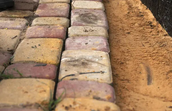 Siyah su geçirmez temellerin yakınındaki kum tabanına taş döşenmiş. Kentsel bahçe inşaatı, patika tesisatı, bina yenileme..