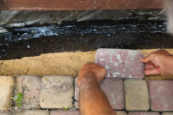 İşçi, su geçirmez temellerin yanındaki kum tabanına elle taş döşüyordu.