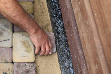 Su geçirmez bir temel duvarı boyunca kaldırım taşları döşeyen bir adamın yakın çekimi. Açık hava inşaatı, asfalt döşeme ve ev geliştirme kavramı.