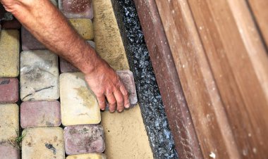 Su geçirmez bir temel duvarı boyunca kaldırım taşları döşeyen bir adamın yakın çekimi. Açık hava inşaatı, asfalt döşeme ve ev geliştirme kavramı.