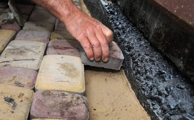 Su geçirmez bir temel duvarı boyunca kaldırım taşları döşeyen bir adamın yakın çekimi. Açık hava inşaatı, asfalt döşeme ve ev geliştirme kavramı.