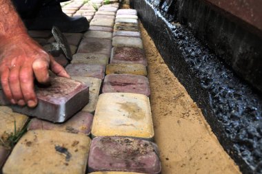 Su geçirmez bir temel duvarı boyunca kaldırım taşları döşeyen bir adamın yakın çekimi. Açık hava inşaatı, asfalt döşeme ve ev geliştirme kavramı.