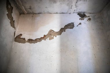 Altına kırmızı tuğla serpiştirilmiş büyük çatlaklar ve kabuk soyma alanları olan eski beyaz bir duvarın yakın çekimi. Yenileme, bozulma, inşaat sorunları ve doku konuları için ideal.