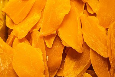 Kurutulmuş mango dilimlerinin bol turuncu renkli ve pürüzsüz desenli makro görüntüsü. Sağlıklı atıştırmalık, tropikal meyve, egzotik yemek ve doğal tatlı temaları için mükemmel..